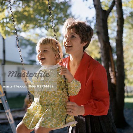 1970s SMILING MOTHER PUSHING LAUGHING GIRL DAUGHTER ON BACKYARD SWING