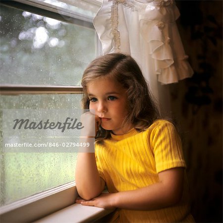 1970s SAD YOUNG GIRL WEARING YELLOW BLOUSE LOOKING OUT WET RAINY WINDOW