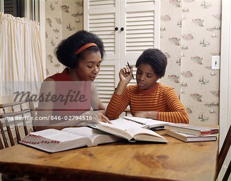 1970s AFRICAN AMERICAN MOTHER AND DAUGHTER DOING HOMEWORK TOGETHER ON KITCHEN TABLE