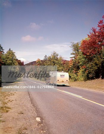 1960s CAR PULLING RV CAMPER DOWN COUNTRY ROAD ADIRONDACKS NEW YORK AUTUMN