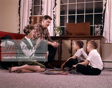 1960s FAMILY WITH TWO SONS GATHERED AROUND RECORD PLAYER LISTENING TO MUSIC INDOOR LIVING ROOM MAN WOMAN BOY