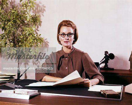 1960s WOMAN BUSINESS WOMAN SEATED DESK SERIOUS EXPRESSION PAPERS EYEGLASSES SECRETARY EXECUTIVE