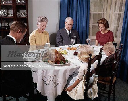 1960s THREE GENERATION FAMILY TOGETHER AROUND HOLIDAY DINNER TABLE SAYING GRACE PRAYER MAN WOMAN BOY GIRL