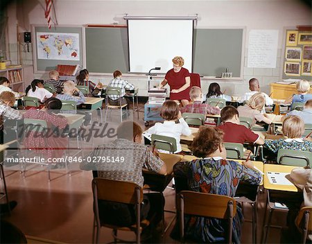 1960s TEACHER WITH CLASS IN SCHOOLROOM WITH AUDIO VISUAL MACHINE EQUIPMENT