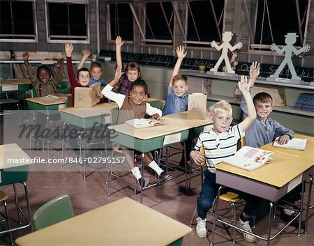 1960s ELEMENTARY SCHOOL CHILDREN IN CLASSROOM WITH HANDS RAISED TO ANSWER QUESTION