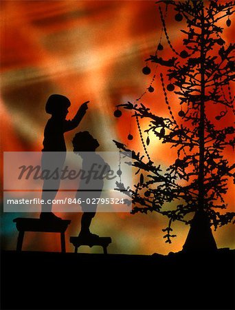 1920s 1930s SILHOUETTE OF 2 CHILDREN ON STOOLS LOOK TO POINTING AT CHRISTMAS TREE COLORFUL LIGHTS BACKGROUND