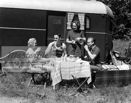 1930s TWO COUPLES EATING PICNIC LUNCH BESIDE CAMPING TRAILER