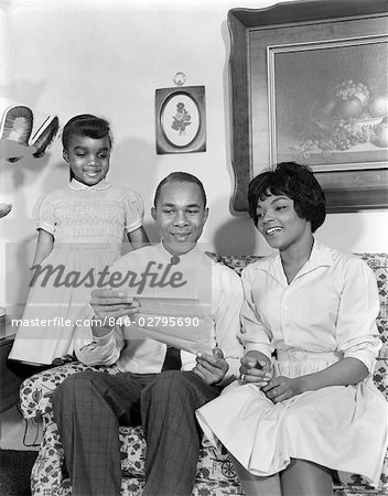 1960s AFRICAN AMERICAN FAMILY ON COUCH READING LETTER OR INSURANCE POLICY MOTHER FATHER DAUGHTER 1960s AFRICAN AMERICAN FAMILY ON COUCH READING LETTER OR INSURANCE POLICY MOTHER FATHER DAUGHTER