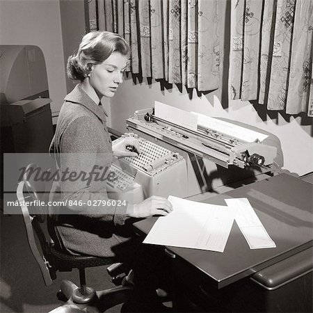 1950s SECRETARY SITTING AT DESK READING FROM LEDGER MAKING ENTRIES ON COMPTOMETER