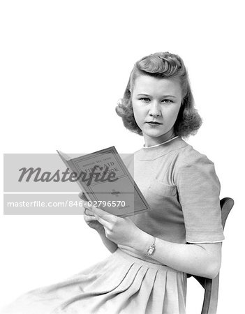 1940s WOMAN SEATED FACING VIEWER WHILE HOLDING A BOOK ENTITLED FIRST AID TEXTBOOK