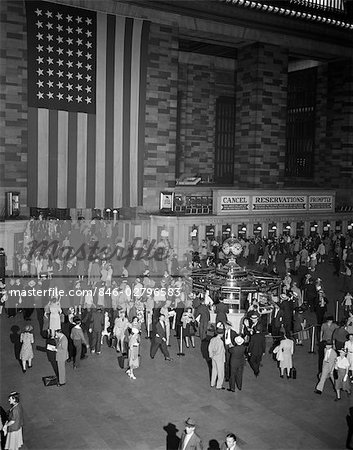 1940s CROWD GRAND CENTRAL STATION LARGE AMERICAN FLAG HANGING ON WALL TICKET WINDOWS INFORMATION BOOTH COMMUTERS TRAVEL