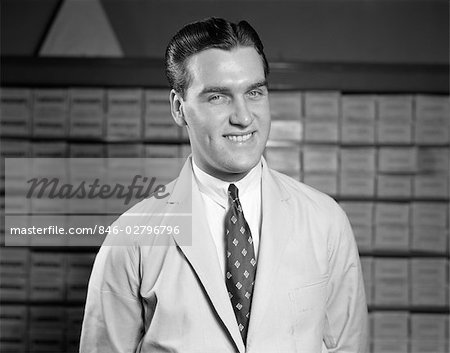 1940s 1950s SALESMAN IN WHITE COAT AND TIE SMILING PORTRAIT PHARMACIST INVENTORY IN BACKGROUND