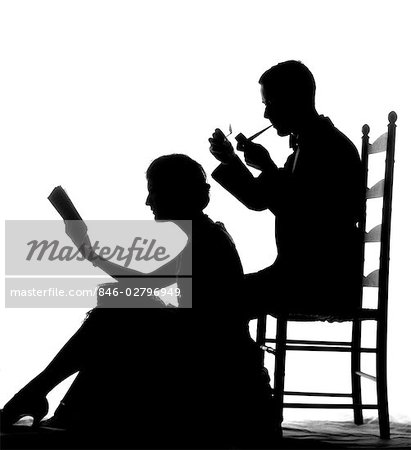 1930s SILHOUETTE OF MAN IN LADDER-BACK CHAIR SMOKING PIPE WITH WOMAN SEATED ON FLOOR IN FRONT OF HIM READING BOOK
