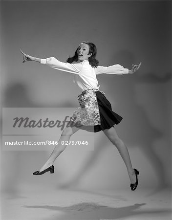 1960s WOMAN HOUSEWIFE WEAR APRON JUMP JUMPING IN AIR BLACK SKIRT WHITE BLOUSE HAPPY SMILING JOY GOOFY WACKY EXPRESSION CHARACTER