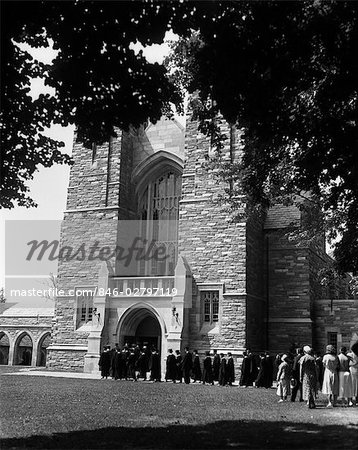 1930s LINE OF GRADUATES FILING INTO LARGE STONE CAMPUS BUILDING