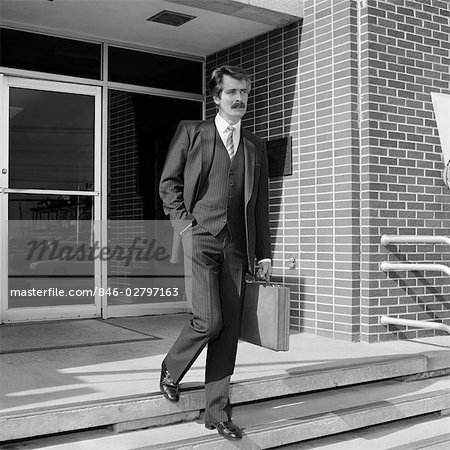 1980s BUSINESSMAN IN PINSTRIPE SUIT WALKING OUT OF BUILDING DOWN STAIRS CARRYING BRIEFCASE