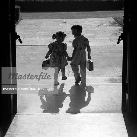 1950s SILHOUETTED BOY GIRL HOLDING HANDS LEAVING SCHOOL DOORS GOING HOME END OF DAY SHADOWS AFTERNOON FRIENDS FRIENDSHIP