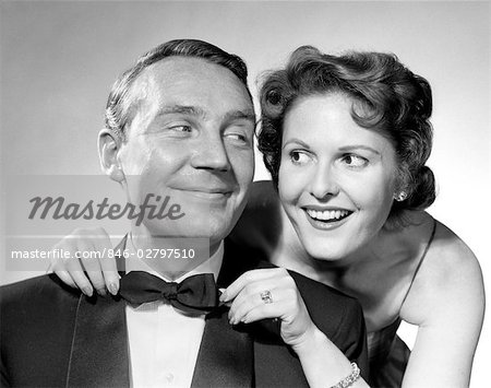 1950s COUPLE DRESSED IN FORMAL ATTIRE WOMAN PULLING ON MAN'S BOWTIE