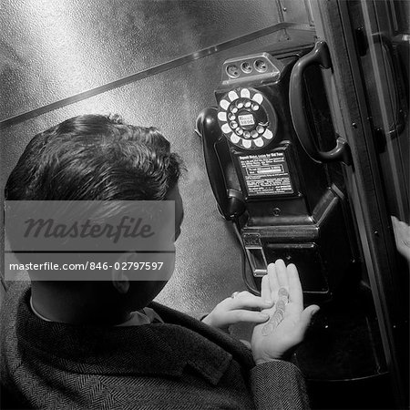 1940s 1950s MAN COUNTING CHANGE IN HAND IN PUBLIC TELEPHONE BOOTH