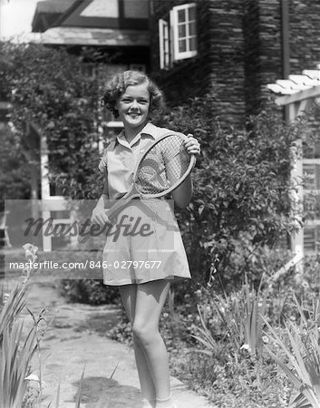1930s TEEN GIRL BRUNETTE ON SIDEWALK OF HOUSE HOLDING TENNIS RACKET RACQUET WEAR SHORTS STRIPED OUTFIT SUMMER