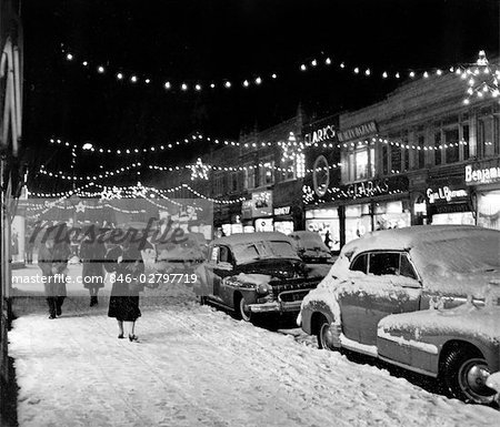 1940s 1950s WINTER CITY STREET SCENE WITH PEDESTRIANS IN SNOW CHRISTMAS LIGHTS