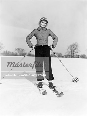 1940s SMILING WOMAN ON SKIS WITH CAP AND QUILTED SKI JACKET WITH BOTH HANDS ON HIPS