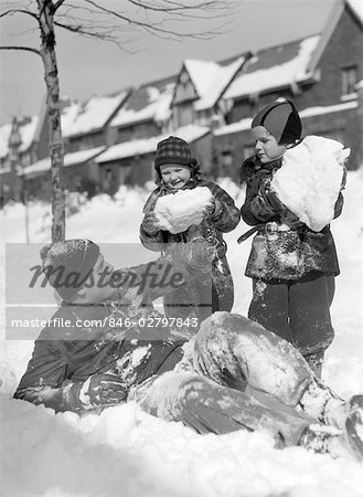 1930s 1940s MAN FATHER TWO CHILDREN PLAYING IN WINTER SNOW FATHER LYING DOWN IN SNOW KIDS HOLD HUGE SNOW BALLS FUN