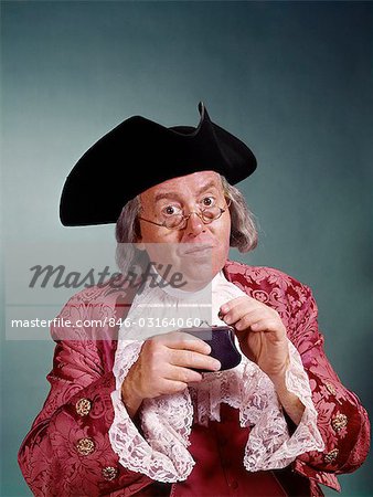 MAN WEARING 18TH CENTURY BEN FRANKLIN COSTUME TRICORN HAT GLASSES DROPPING A PENNY INTO SMALL COIN PURSE