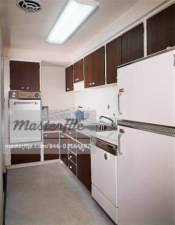 1970s NARROW GALLEY STYLE KITCHEN WITH DARK WOODEN CABINETS AND WHITE APPLIANCES