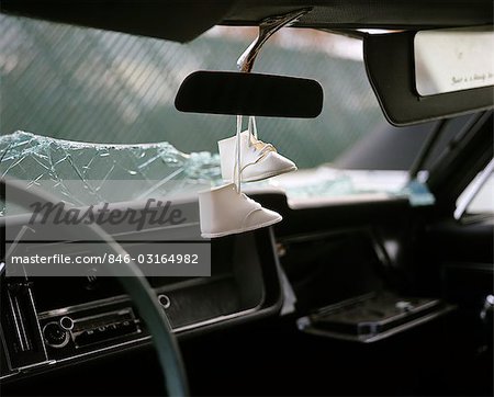 1960s 1970s PAIR WHITE BABY SHOES DANGLING FROM REAR VIEW MIRROR OF WRECKED CAR WITH SHATTERED GLASS WINDSHIELD