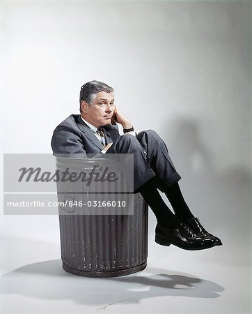 1960s SAD MAN IN BUSINESS SUIT SITTING IN TRASH GARBAGE CAN