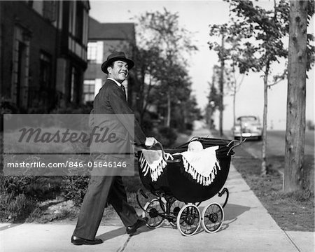 1940s - 1950s SMILING FATHER IN SUIT & HAT PUSHING BABY IN CARRIAGE DOWN SIDEWALK