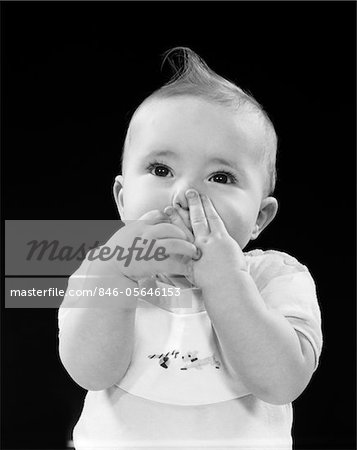 1950s PORTRAIT OF BABY COVERING MOUTH WITH HANDS FINGERS