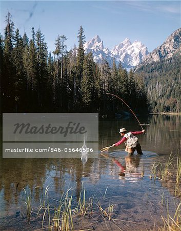 1970s MAN FISHERMAN RED SHIRT IN ROCKY MOUNTAINS STREAM LAKE FLY ROD CATCH SPLASHING ON LINE NET
