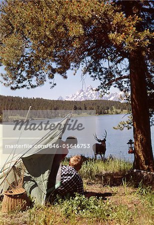 1950s GRAND TETON NATIONAL PARK WYOMING TWO CHILDREN IN TENT LOOKING AT DEER BY LAKE