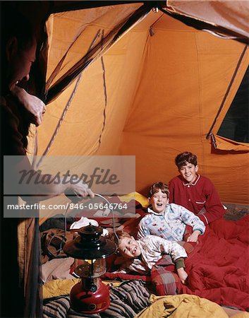 1960s FATHER WITH LANTERN CHECKING UP ON 3 BOYS IN SLEEPING BAGS PAJAMAS IN TENT