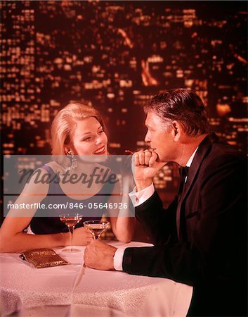1960s - 1970s SMILING ROMANTIC COUPLE MATURE MAN BLOND WOMAN IN FORMAL EVENING DRESS IN A NIGHTCLUB DRINKING CHAMPAGNE