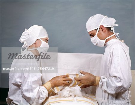 1950s - 1960s DOCTOR & NURSE IN SURGERY OPERATION OPERATING STERILE SURGICAL WHITE CAPS GOWNS MASKS