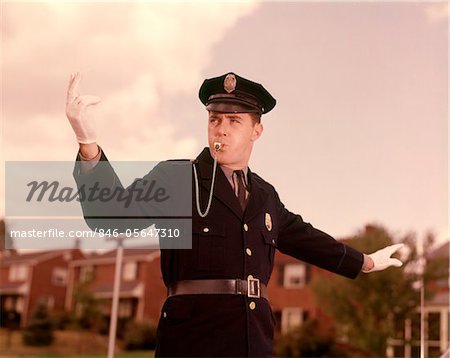 1960s MAN POLICEMAN BLOWING WHISTLE DIRECTING TRAFFIC