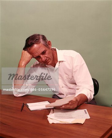 1970s MIDDLE AGE MAN SITTING AT DESK WORRIED ABOUT BILLS TO PAY