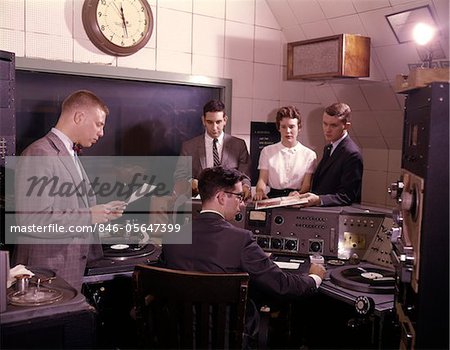 1960s GROUP OF 5 PEOPLE IN RADIO STATION CONTROL ROOM DISK JOCKEY DJ TURNTABLES BROADCASTING MEDIA COMMUNICATIONS