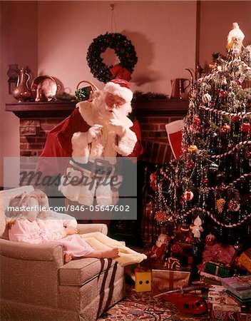 1960s SANTA LOOKING DOWN ON TWO CHILDREN BOY GIRL ASLEEP IN CHAIR BY FIREPLACE CHRISTMAS TREE