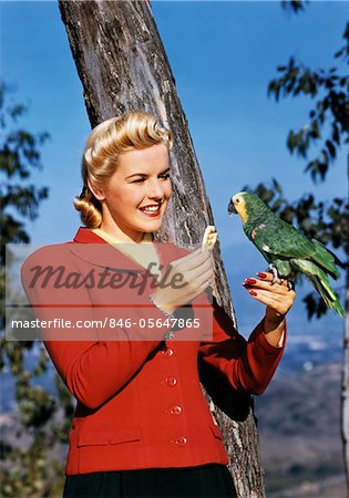 1940s SMILING BLOND WOMAN FEEDING CRACKER TO PARROT OUTDOORS