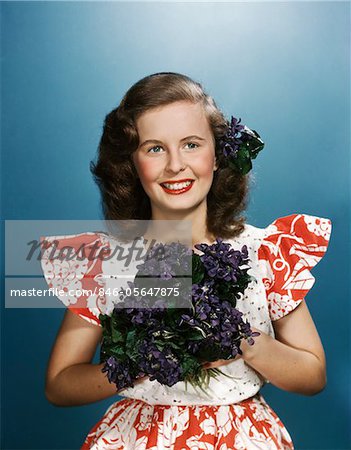 1940s - 1950s SMILING YOUNG WOMAN WEARING RED AND WHITE DRESS HOLDING BOUQUET OF VIOLETS
