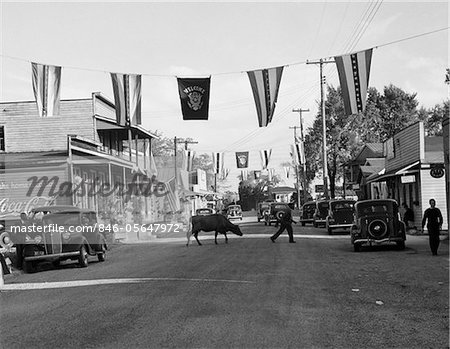 1930s MAIN STREET SMALL TOWN WITH FLAGS FLYING & COW CROSSING STREET