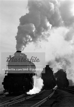 1930s - 1940s HEAD-ON VIEW OF THREE STEAM ENGINES SILHOUETTED AGAINST BILLOWING SMOKE AND STEAM OUTDOOR