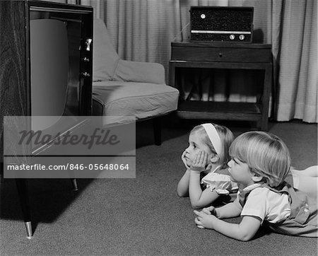 1960s - 1970s TWO TODDLERS BOY GIRL LYING ON FLOOR WATCHING TELEVISION