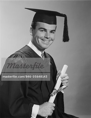 1960s SMILING MAN HOLDING DIPLOMA WEARING GRADUATION ROBES