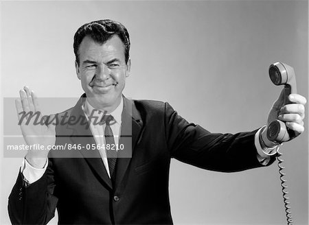 1960s BUSINESSMAN HOLDING TELEPHONE AT ARMS LENGTH WITH EXPRESSION OF DISGUST OR REJECTION