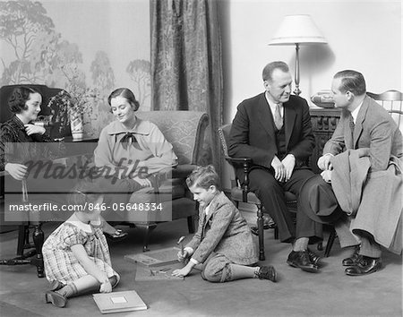 1930s FAMILY MOTHER FATHER TWO KIDS PLAYING ON FLOOR VISITING WITH ANOTHER COUPLE